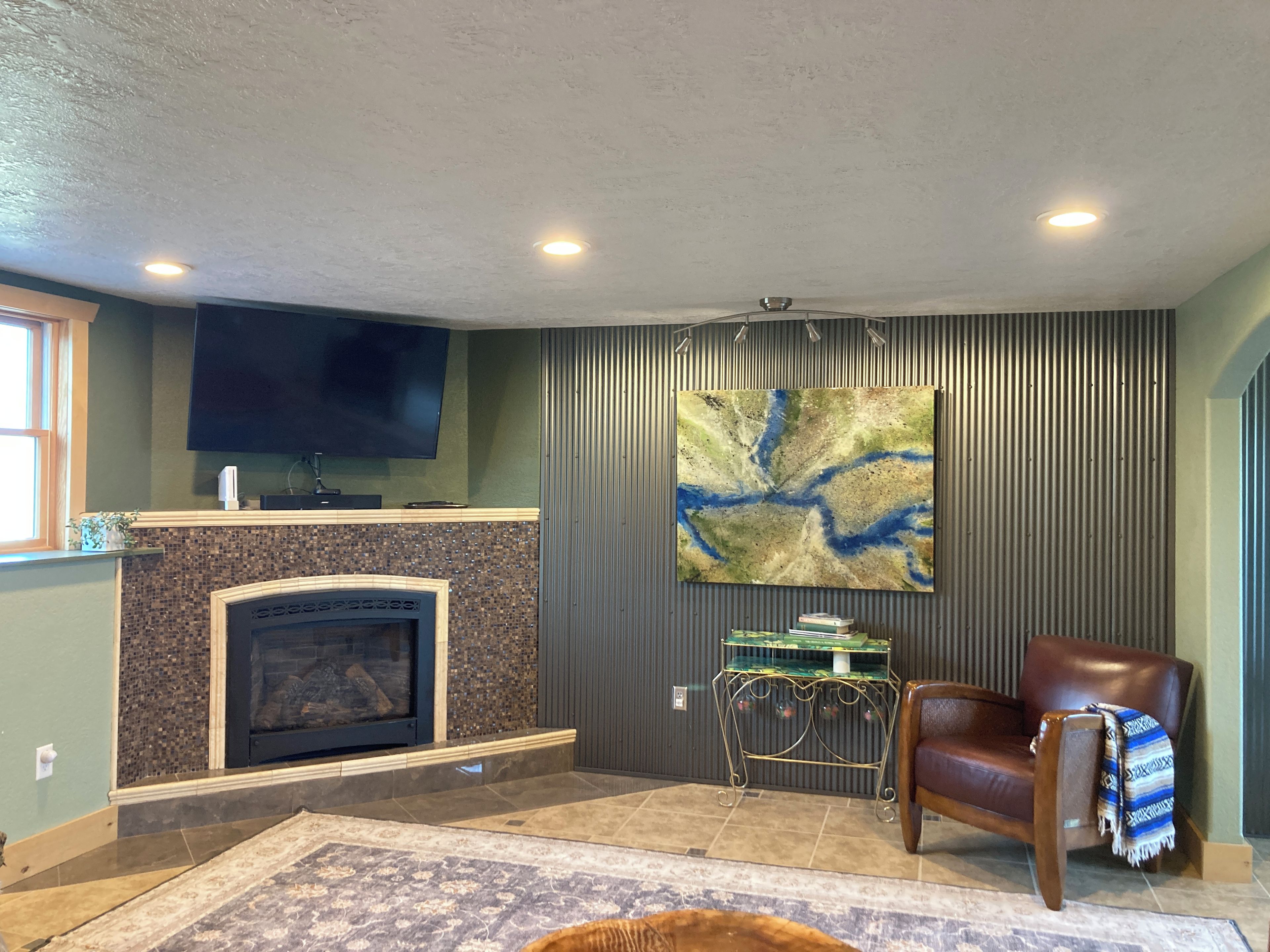 Una sala de estar con chimenea, televisor montado, un cuadro abstracto grande y un sofá de cuero.
