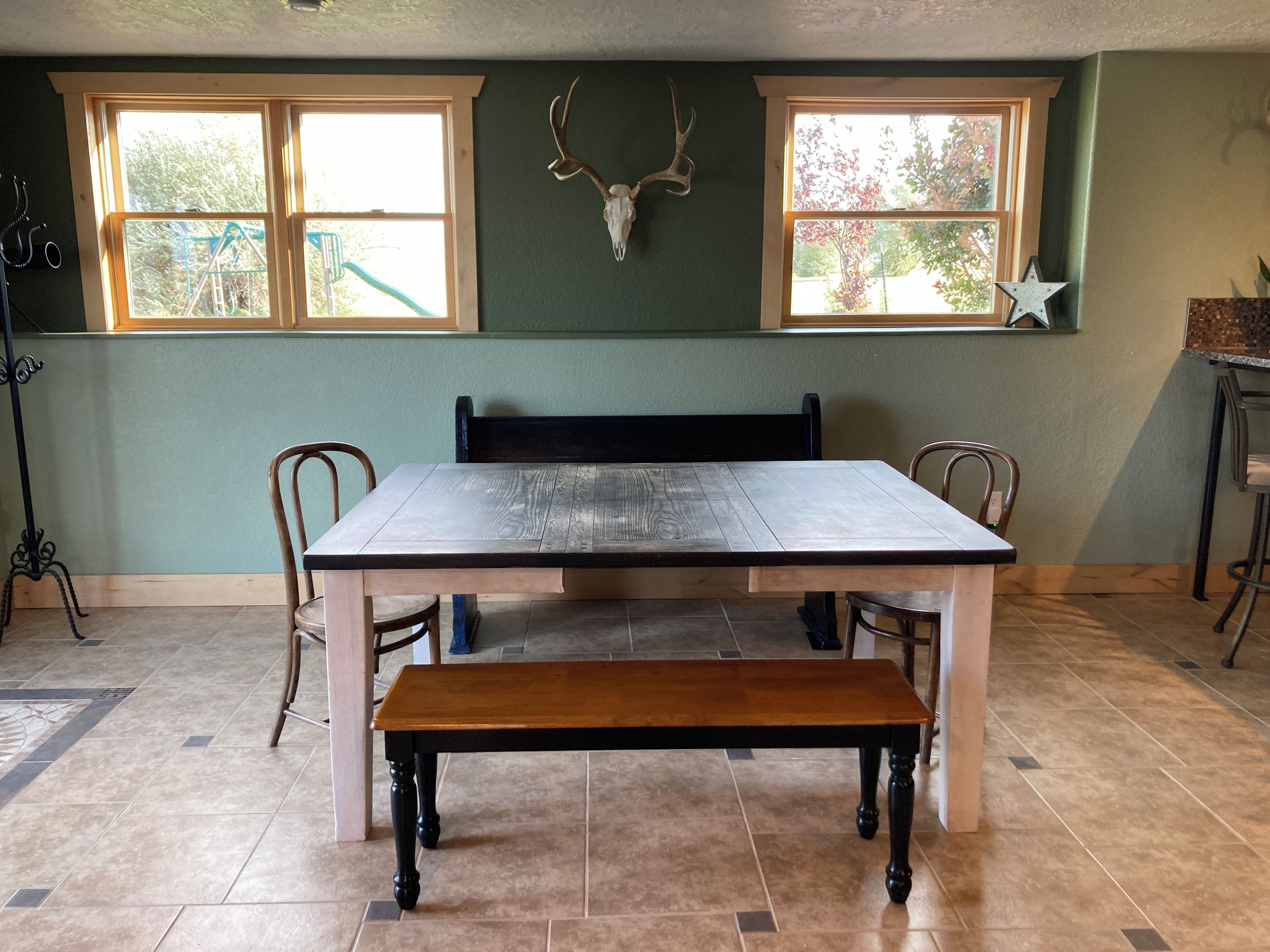 A dining area with a wooden table, chairs, a bench, and a wall-mounted deer skull.