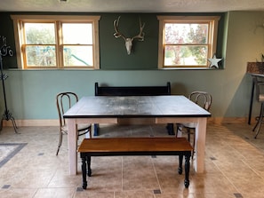 A dining area with a wooden table, chairs, a bench, and a wall-mounted deer skull.