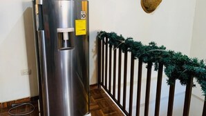 A stainless steel refrigerator next to a wooden railing with a deer head mounted on the wall. - Casa Sucursal del Cielo (Concepción de Ataco)