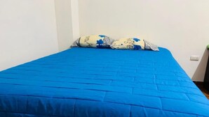 A bed with a blue quilt and a floral-patterned pillow in a room with white walls. - Casa Sucursal del Cielo (Concepción de Ataco)