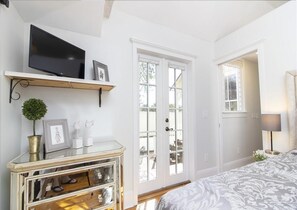 A bedroom with a bed, a TV on a shelf, a door with glass panels, and a window with blinds.