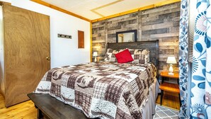 Una camera da letto con una testiera in legno, una coperta trapuntata, una panca ai piedi del letto, un comodino con una lampada e uno specchio appeso al muro.