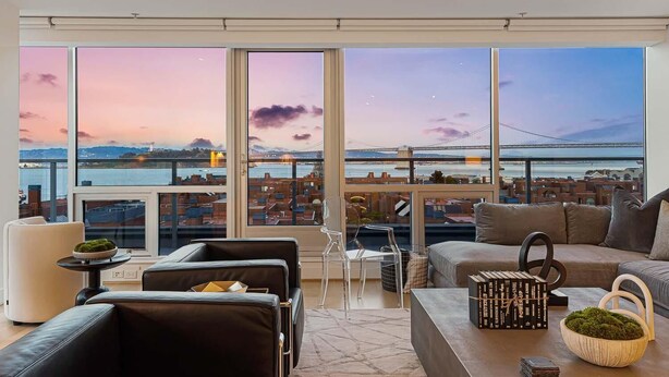 A modern living room with a large view of a cityscape and a bridge at sunset.