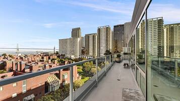 En hög byggnad med en balkong som vetter ut mot en stadsbild, med modern arkitektur och fri utsikt över staden och en bro i fjärran.