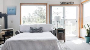Un dormitorio con cama, mesita de noche, lámpara y vistas al exterior.