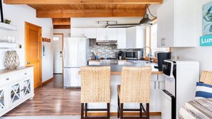 Una cocina moderna con armarios blancos, una isla central y un microondas. Hay dos sillas de mimbre junto a la isla.