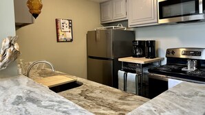 A modern kitchen with a stainless steel refrigerator, a microwave, a stove, and a coffee maker. - 1st Floor 1BR/1BA Condo w/ Pool: Golf, Swim & Casino nearby! Sunshine Oaks (Diamondhead)