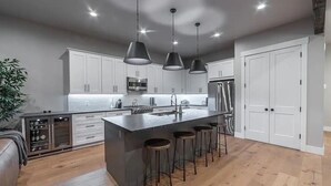 A modern kitchen with white cabinets, stainless steel appliances, and a central island with bar stools. - Whitefish Lynx Run Town House Private Hot Tub (Whitefish)
