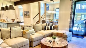 A modern living room with a sectional sofa, a round coffee table, and a staircase leading to an upper level. - Whitefish Lynx Run Town House Private Hot Tub (Whitefish)