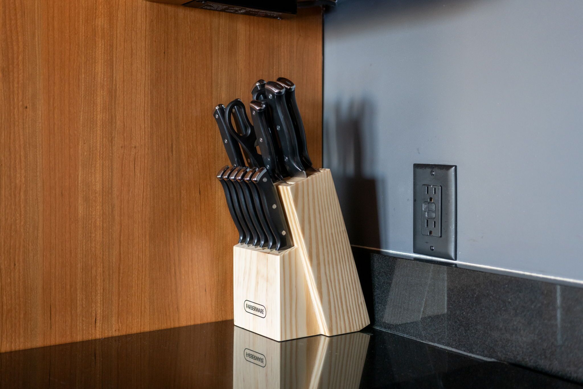A kitchen counter with a knife block and an electrical outlet.