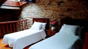 A room with two single beds, wooden headboards, a stone wall, and a small table with a vase of flowers. - Casa Pacios By M De Santiago (Triacastela)