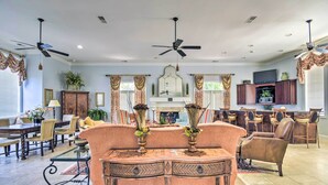 Amplia sala de estar con comedor, dos ventiladores de techo, chimenea y zona de cocina con taburetes de bar.