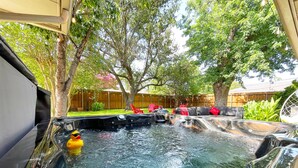 Ein Whirlpool mit einem gelben Quietscheentchen, umgeben von Gartenmöbeln und Bäumen.