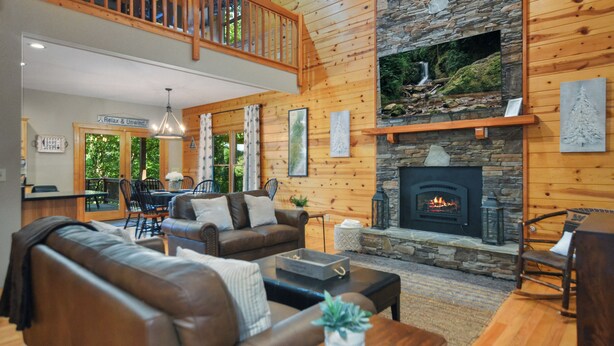 Un intérieur de chalet chaleureux avec une cheminée en pierre, des murs en bois et un balcon.