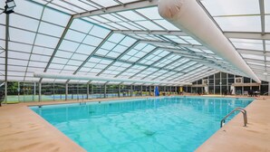 Une piscine intérieure dotée d’un toit en verre, entourée d’une terrasse en béton.