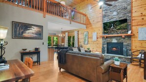 Un vaste espace de vie doté d’un plancher en bois, d’un grand canapé, d’une cheminée et d’un balcon.