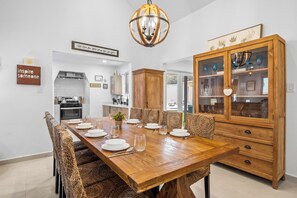 A dining area with a wooden table set for six, surrounded by woven chairs. A wooden cabinet with glass doors is to the right.