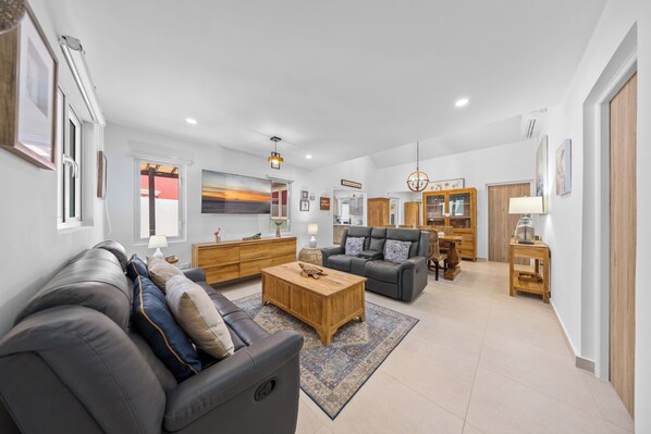 A spacious living room with a sofa, a coffee table, and a dining area with wooden furniture.
