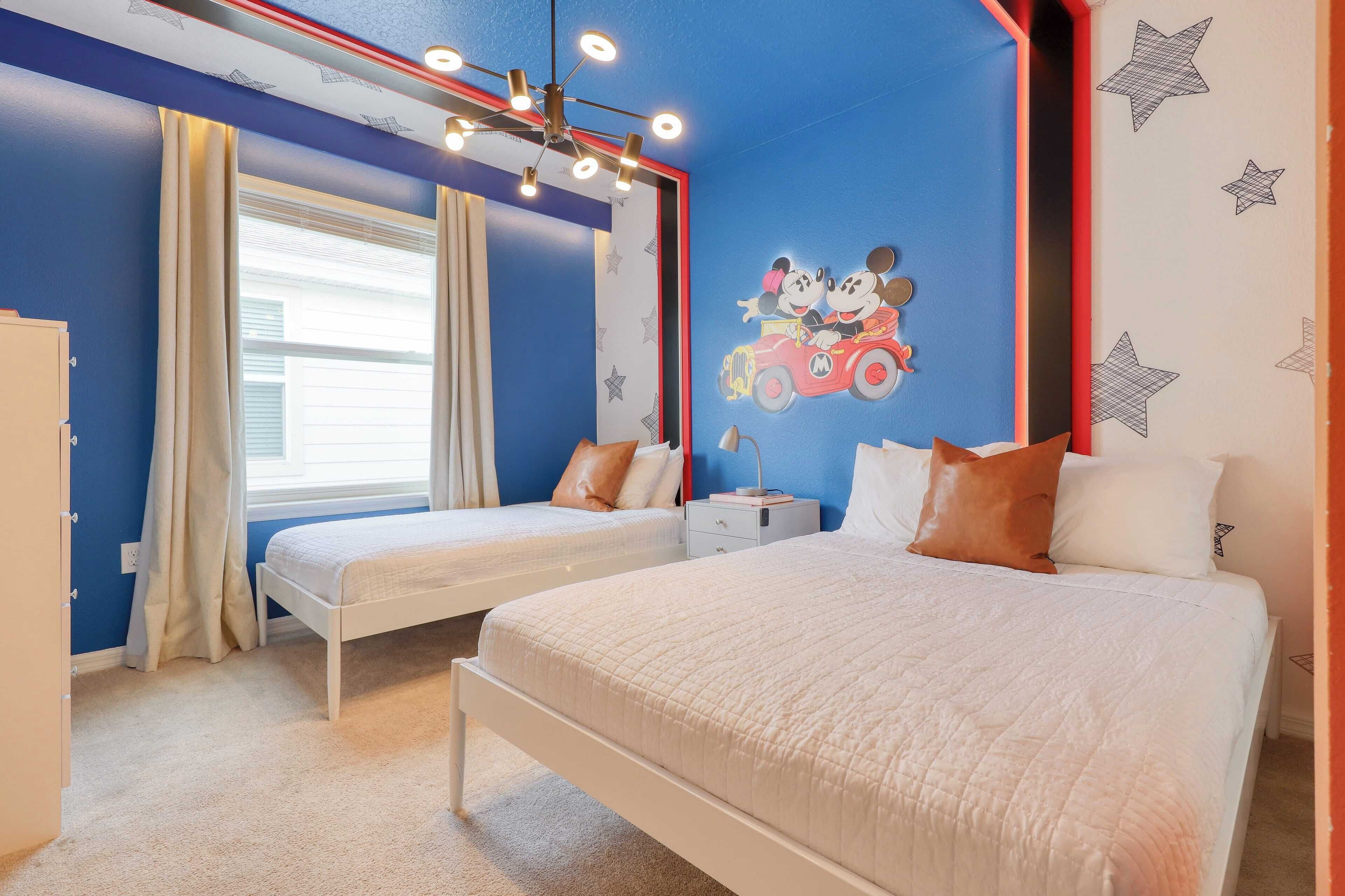 A bedroom with two single beds, a nightstand, a dresser, and a Mickey Mouse mural on the wall.