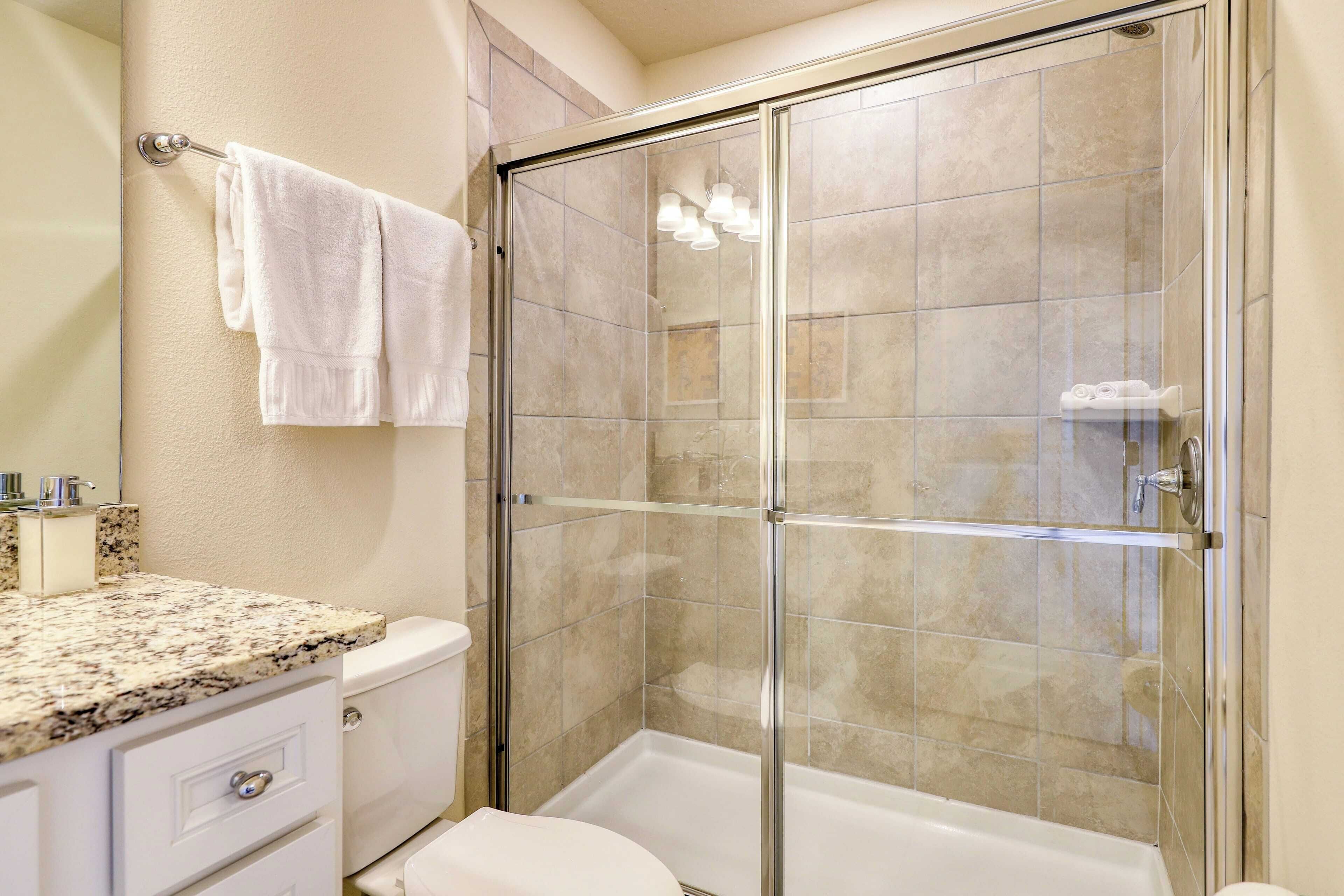 Une salle de bain avec une douche à parois de verre, des toilettes blanches et un comptoir en granit avec un évier.
