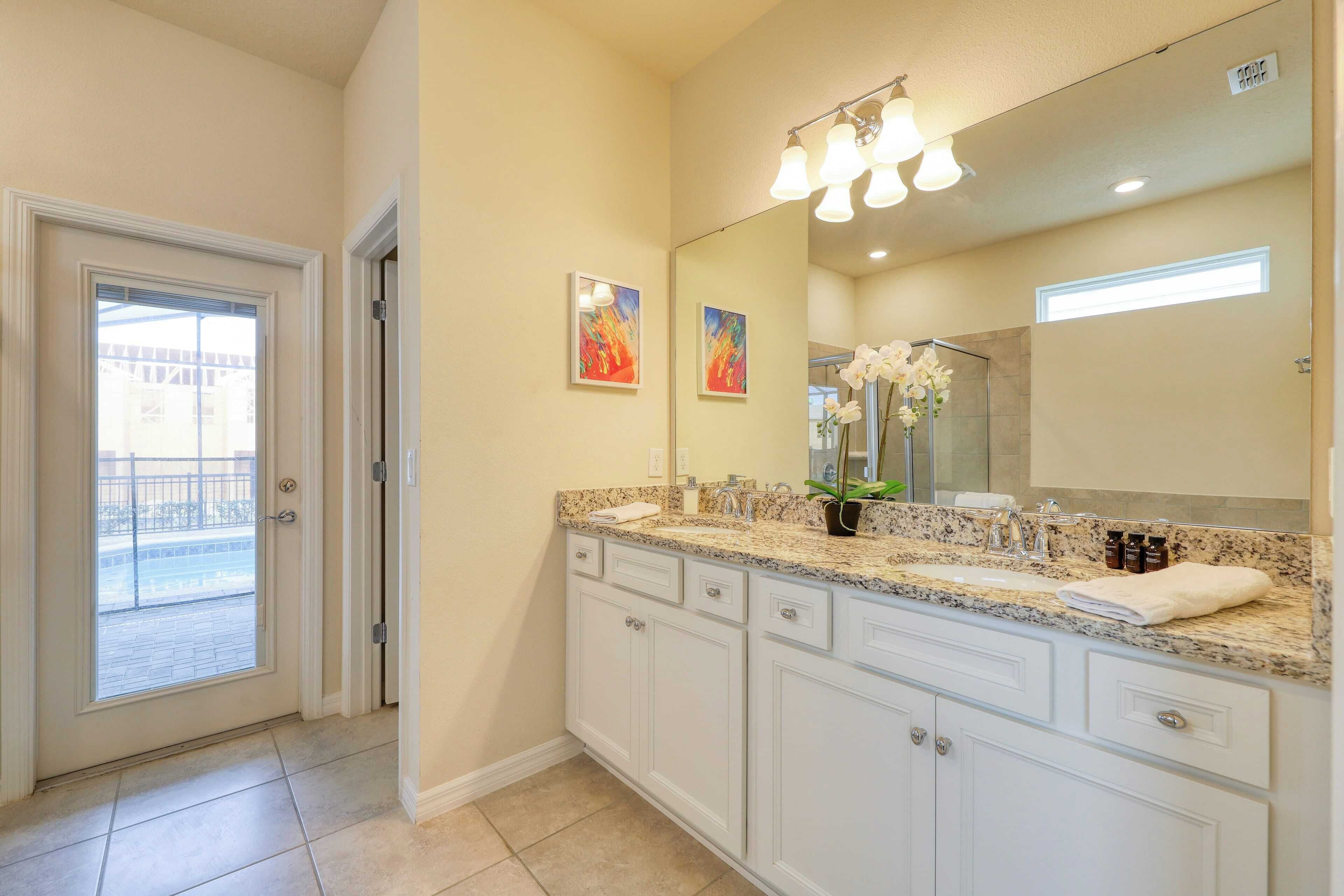 A bathroom with a large mirror, granite countertop, white cabinets, and a potted plant.