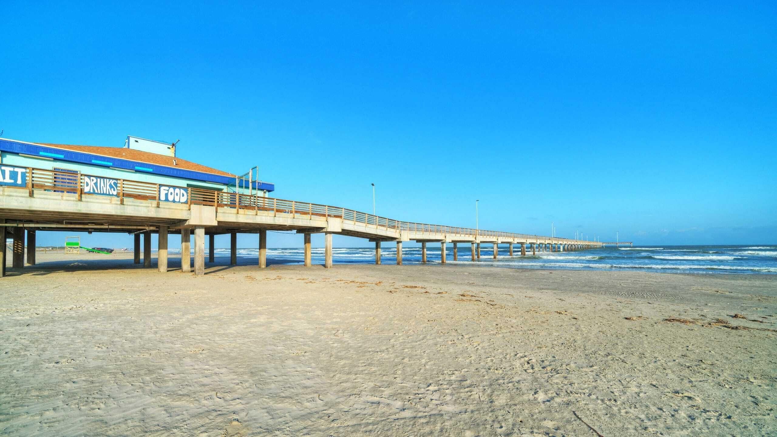 A pier extending into the ocean with a building labeled "Drinks" and "Food" on the side.