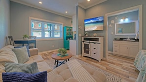 A living room with a sofa, a coffee table, and a TV. There is a kitchen area with cabinets and a sink. - 2 Pools, Beach Boardwalk Access Studio, Sleeps 5 Beach Bungalow by Avantstay (Port Aransas)