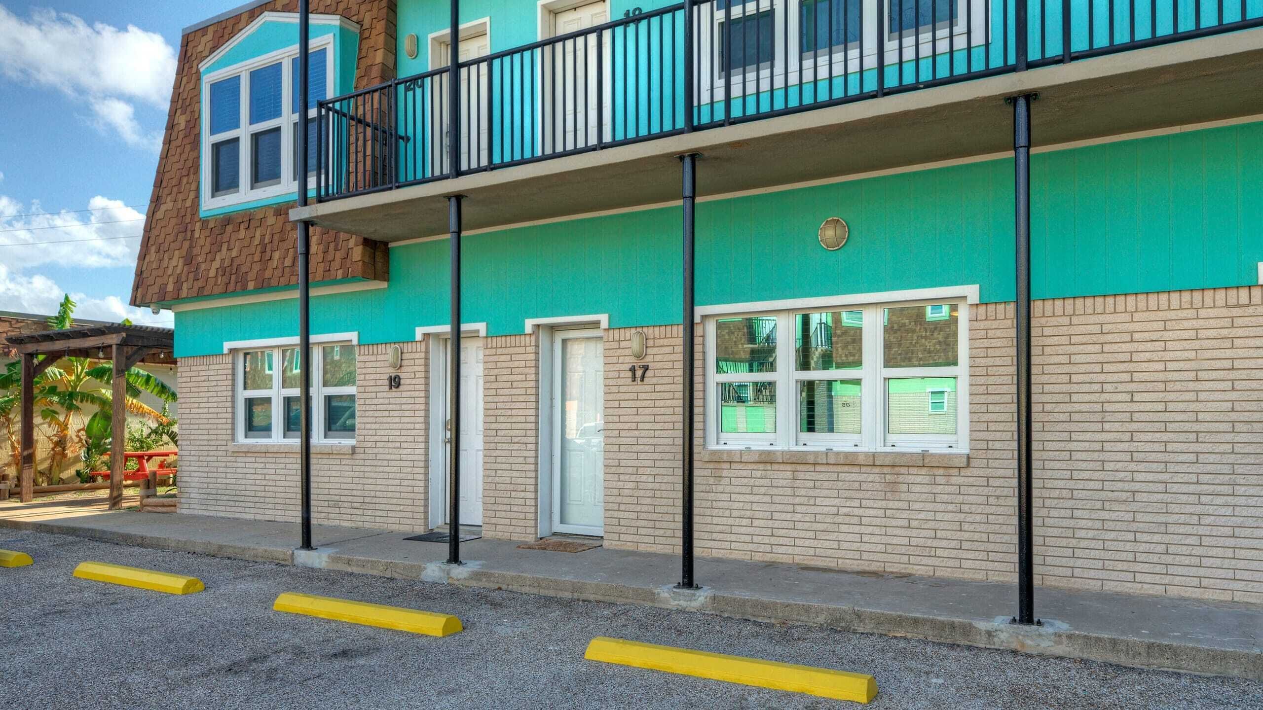 Un edificio de varios pisos con fachada verde, múltiples ventanas y un balcón con barandas negras.