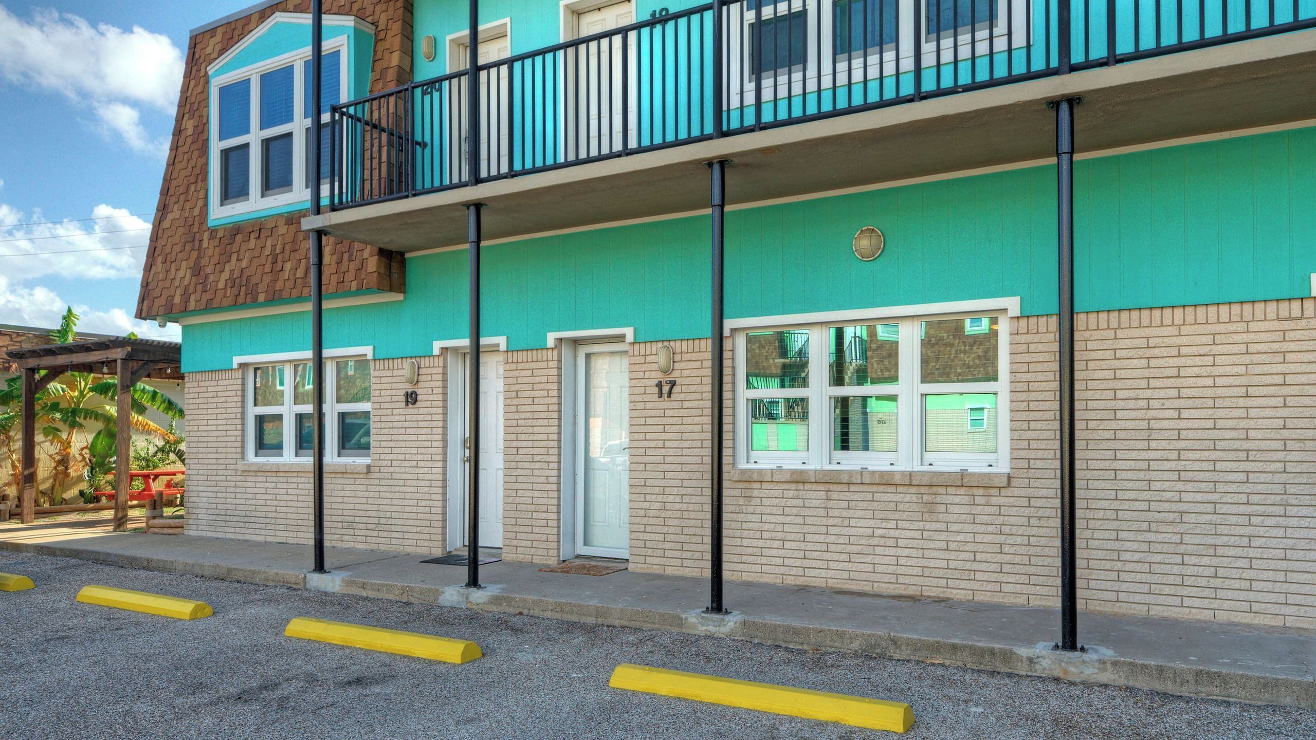 A multi-story building with a green facade, multiple windows, and a balcony with black railings.