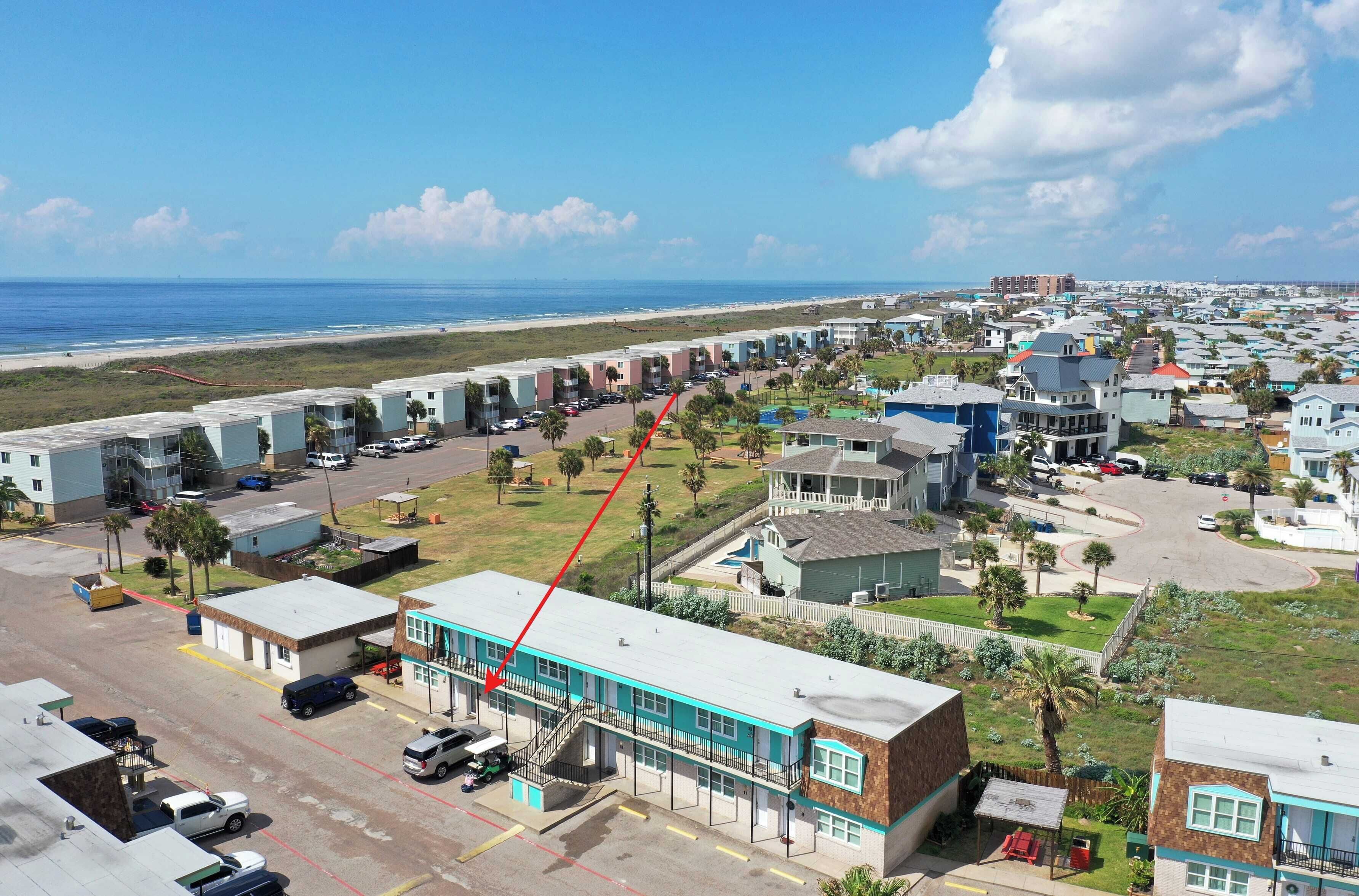 Een kusthotel met een lange rij kamers, een parkeerplaats en uitzicht op het strand.