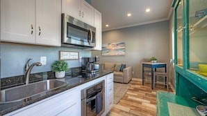 A compact kitchen with a stainless steel sink, a microwave, and a coffee maker. There is a dining area with a table and chairs, and a sofa. A painting is on the wall, and a plant is on the counter. - 2 Pools, Beach Boardwalk Access Studio, Sleeps 5 Beach Bungalow by Avantstay (Port Aransas)