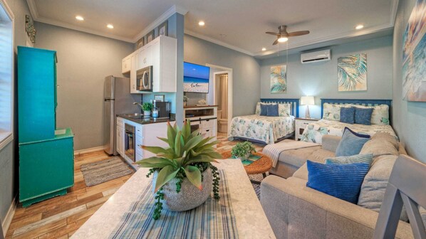 Un espacio habitable compacto con kitchenette, dos camas y ventilador de techo.