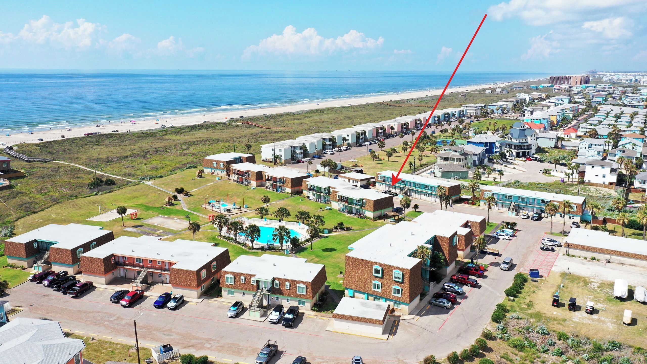 Vue aérienne d’un quartier résidentiel situé sur la côte, avec des propriétés donnant sur la plage, une piscine et un parking.