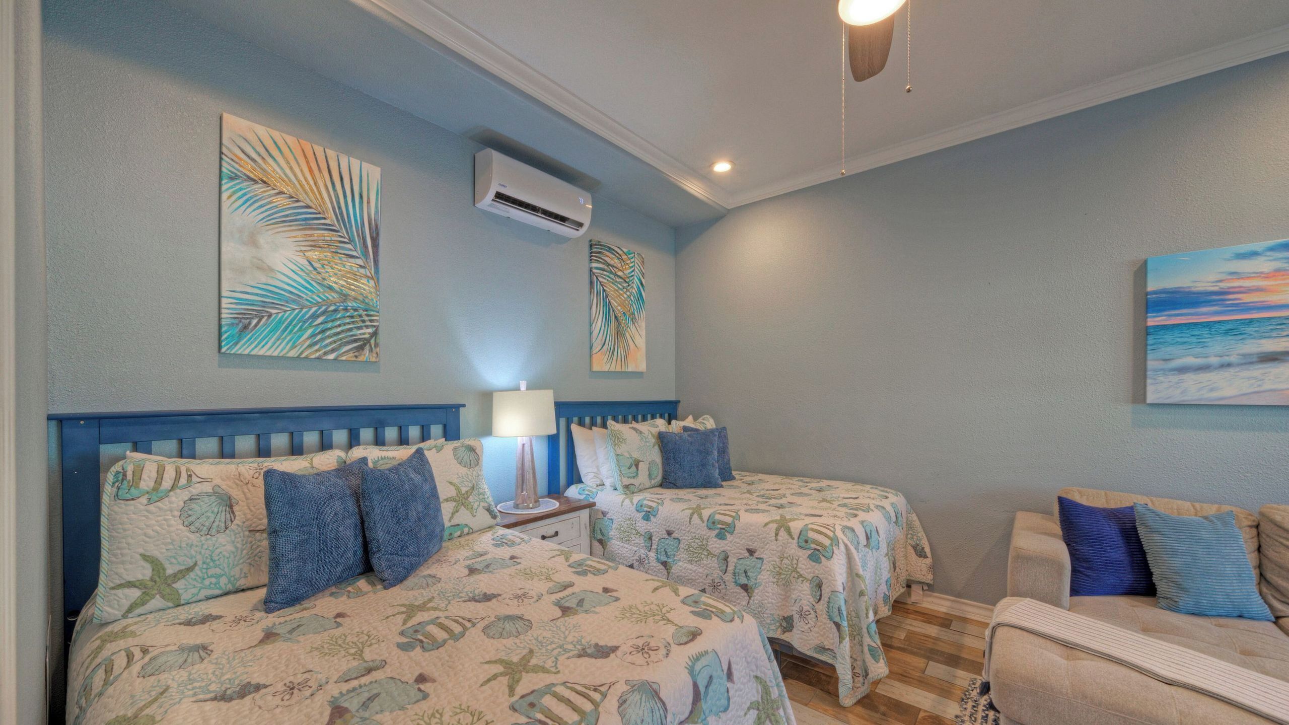 A bedroom with two beds, a nightstand, a lamp, and artwork on the walls.