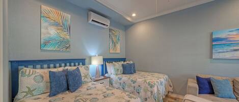 A bedroom with two beds, a nightstand, a lamp, and artwork on the walls.