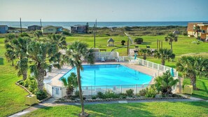 Una piscina con cerca blanca, rodeada de palmeras y vista al océano.