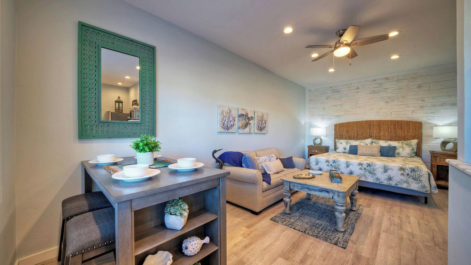 A compact living space with a dining area, a sofa, a bed, and a ceiling fan.