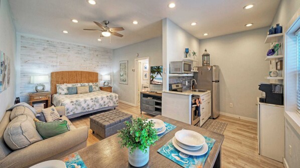 Un espacio habitable compacto con cama, sofá, mesa de comedor, kitchenette y ventilador de techo.