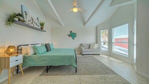 Une chambre à coucher comprenant un lit, une table de chevet, une lampe, un canapé, un ventilateur de plafond, une fenêtre et une étagère murale agrémentée de plantes.