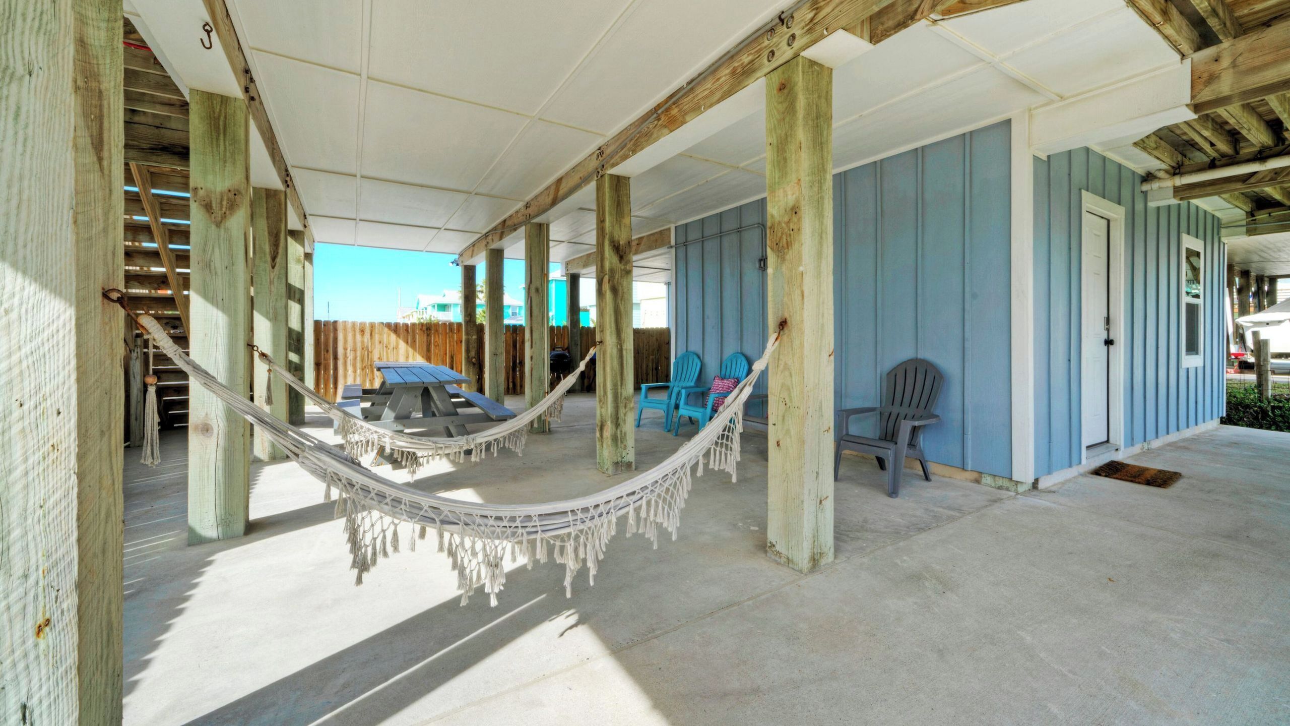A covered outdoor area with a hammock, blue chairs, and a picnic table.