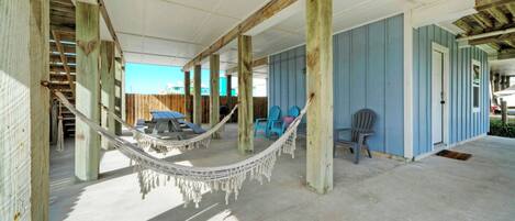 A covered outdoor area with a hammock, blue chairs, and a picnic table.