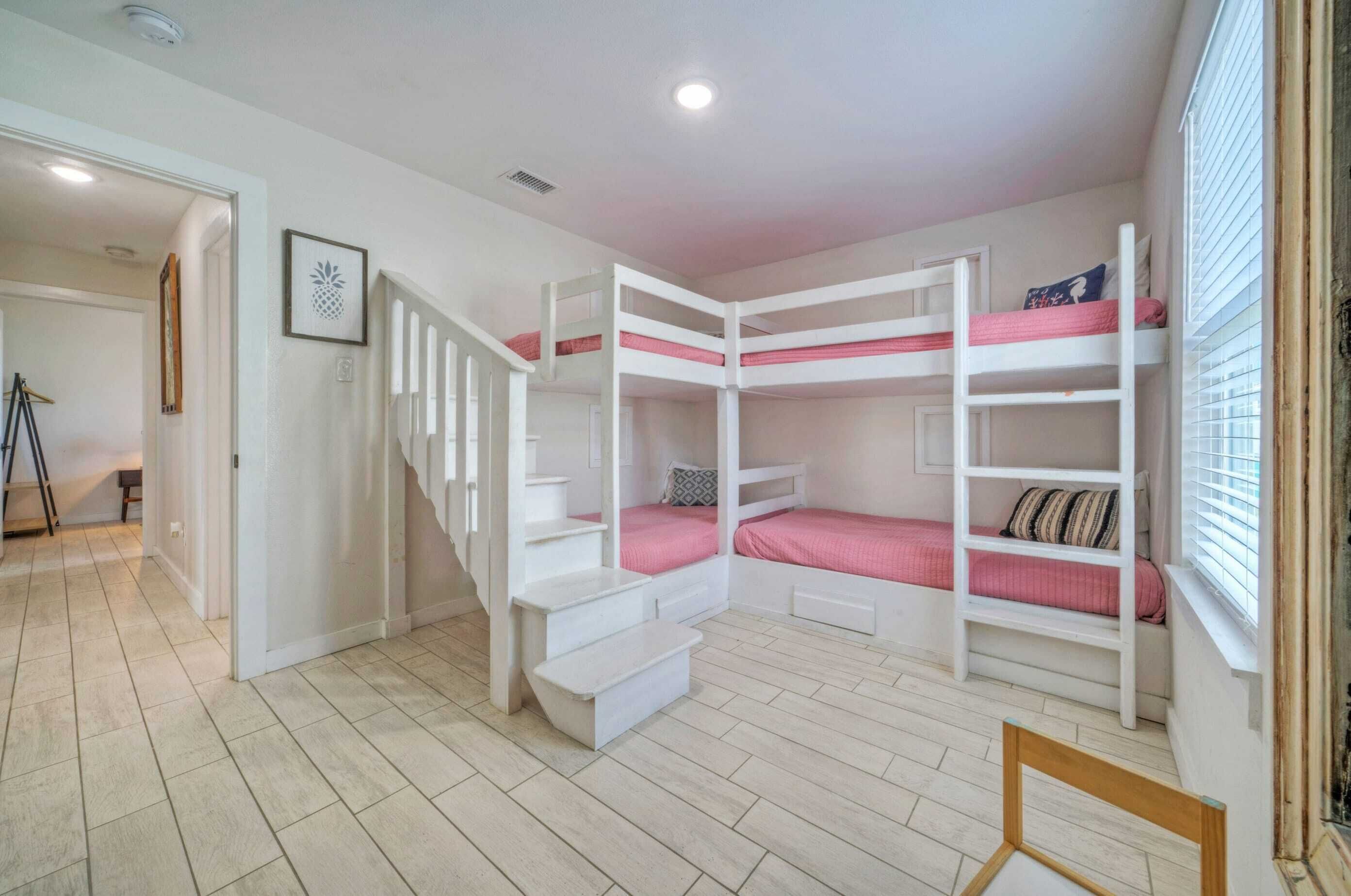 A room with bunk beds, a staircase, and a window with blinds.
