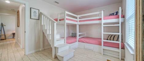 A room with bunk beds, a staircase, and a window with blinds.