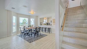 A spacious dining area with a large table and chairs, a kitchen with modern appliances, and a wooden staircase. - Private Pool, Game Room, Patio, Near the Beach Palm House by Avantstay (Port Aransas)