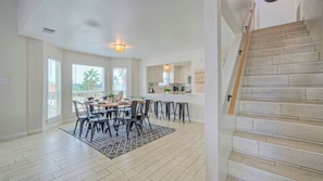 Un vaste espace de salle Ă manger avec une grande table et des chaises, une cuisine Ă©quipĂ©e dâappareils Ă©lectromĂ©nagers modernes et un escalier en bois.