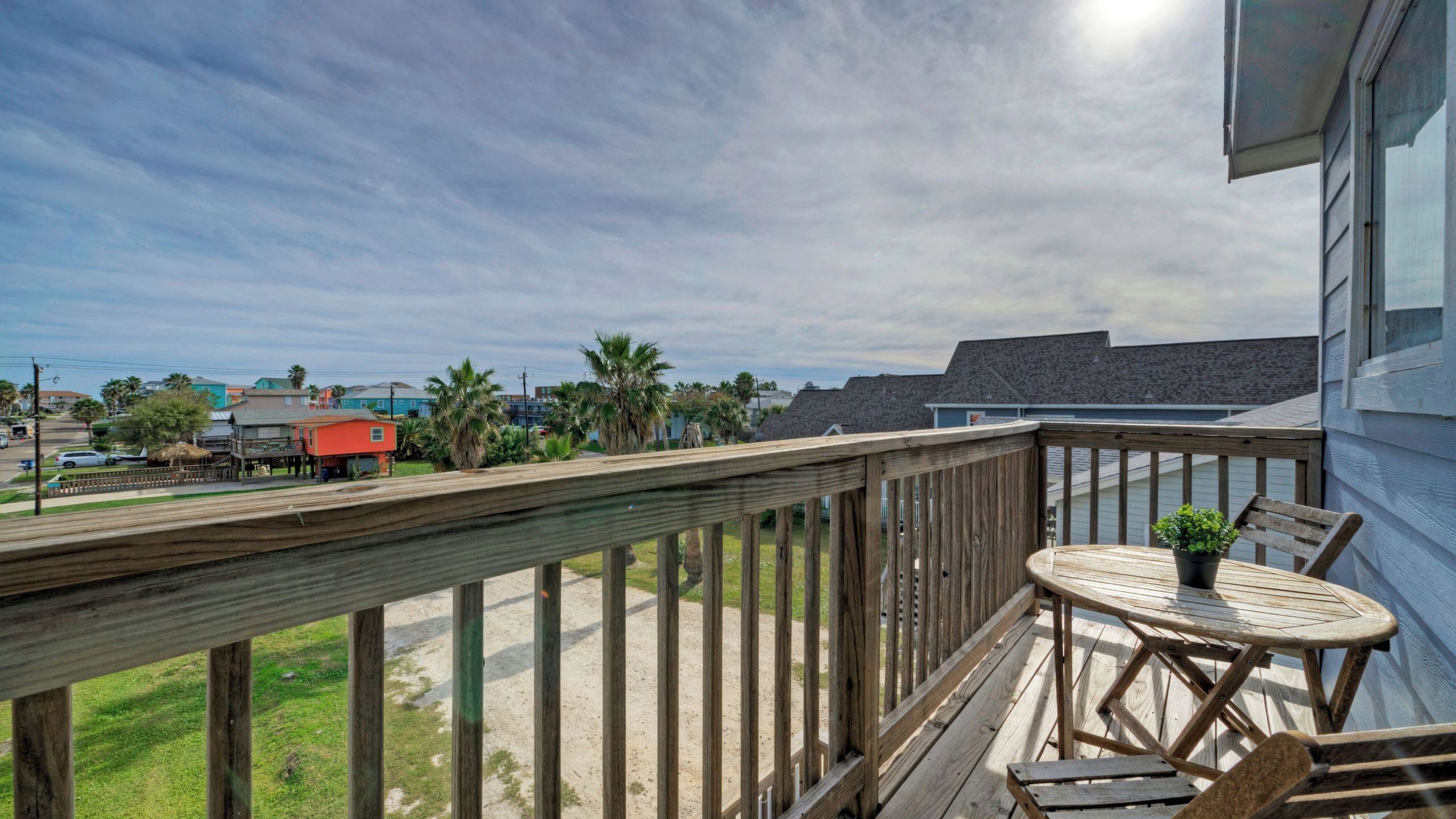 A wooden deck with a table and chairs, overlooking a residential area with houses and palm trees.