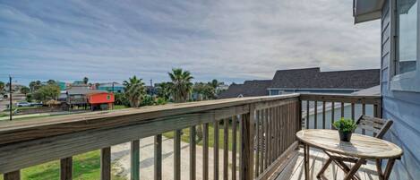 A wooden deck with a table and chairs, overlooking a residential area with houses and palm trees.