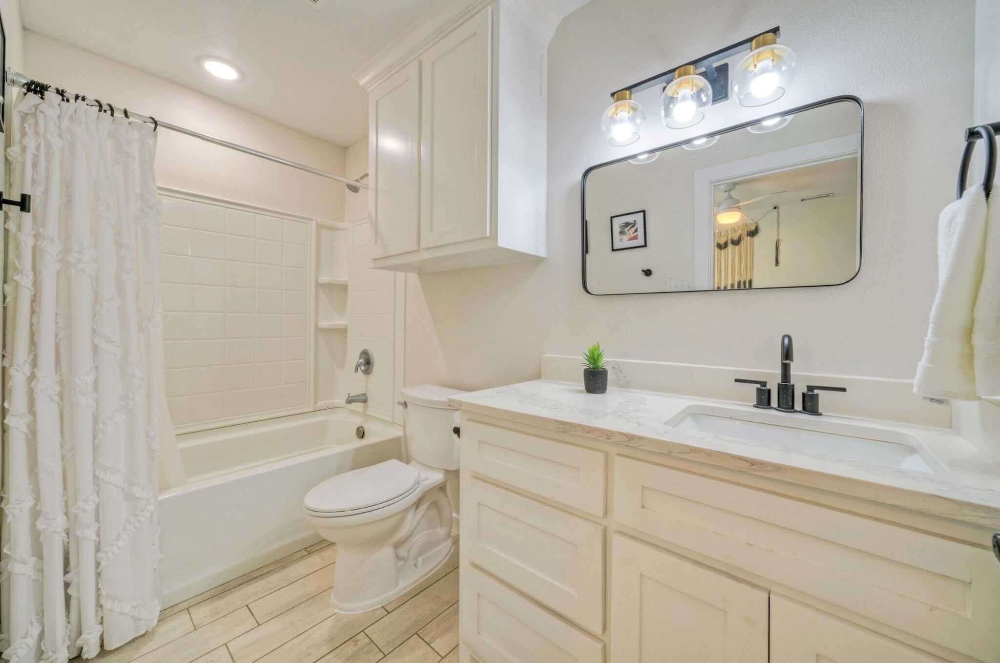 Une salle de bain comprenant une baignoire, des toilettes, un meuble-lavabo avec un miroir et un évier.