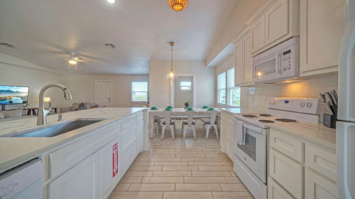 A modern kitchen with white cabinetry, a central island, a dining area with chairs, and a large window providing natural light.